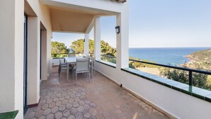 Un balcone con tavolo e sedie, un pavimento piastrellato e vista sul mare e sul paesaggio.