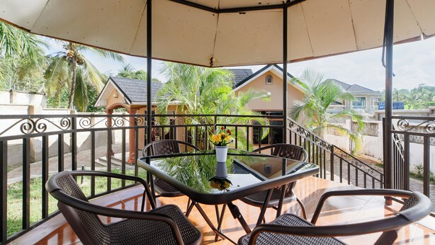 A covered outdoor seating area with a glass table, metal chairs, and a decorative vase.