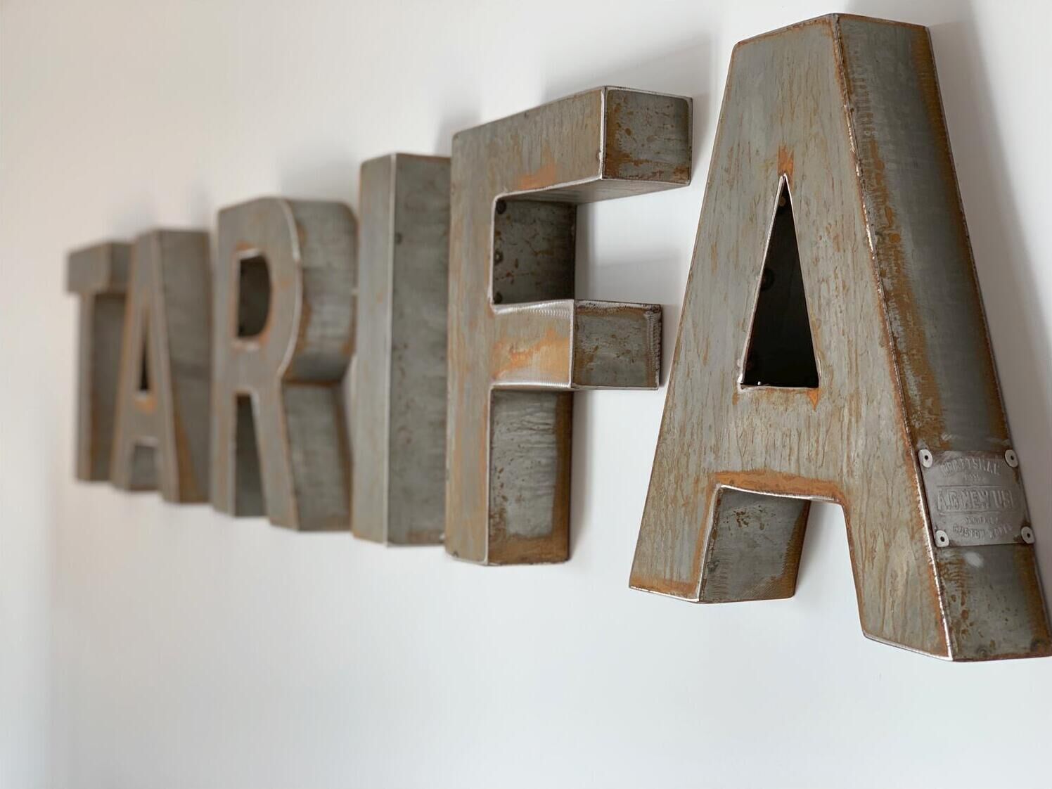 A wall with large, rusted metal letters spelling 'TARIFA.'