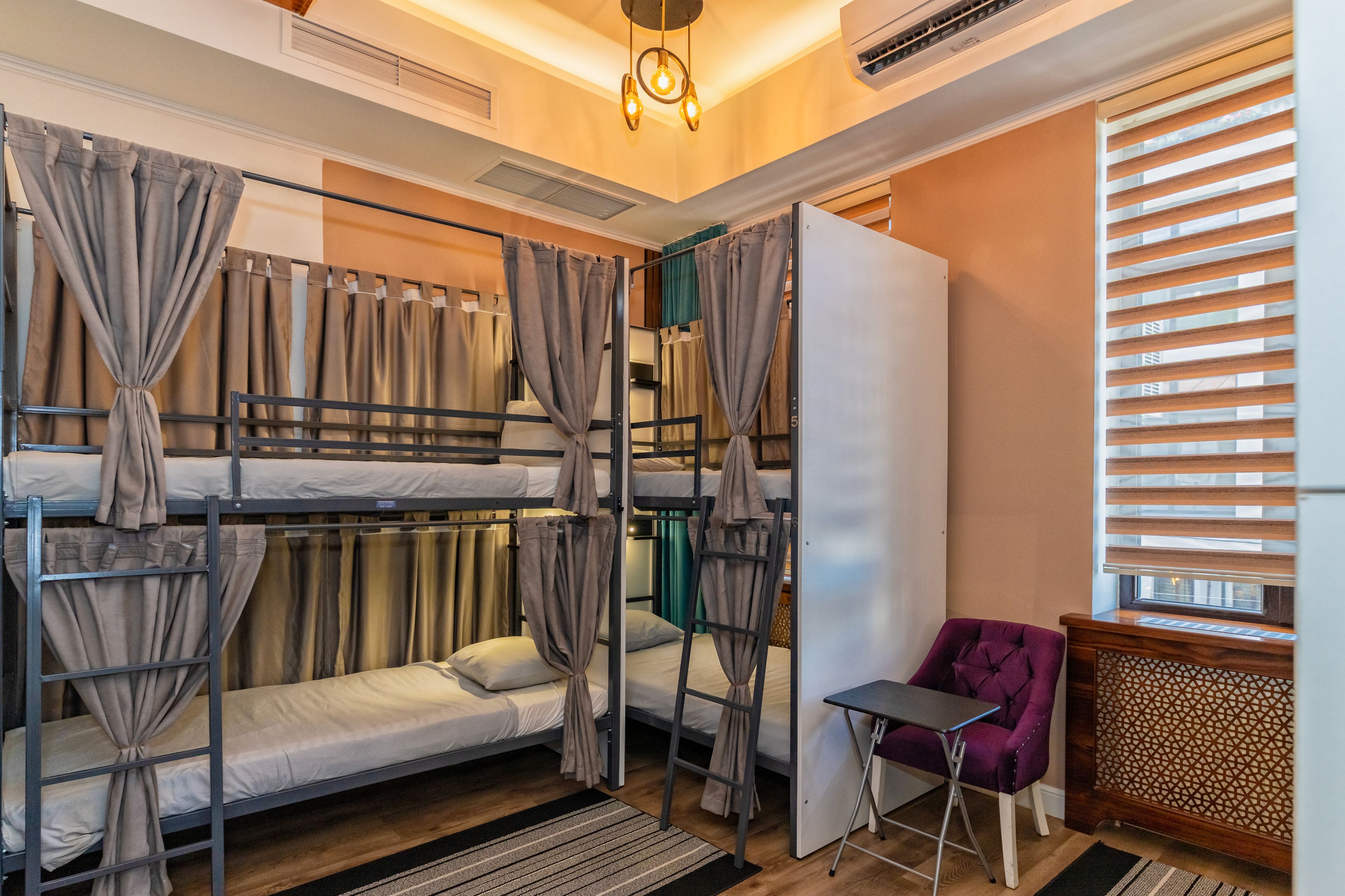 A bunk bed room with curtains, a small table, and a purple chair.