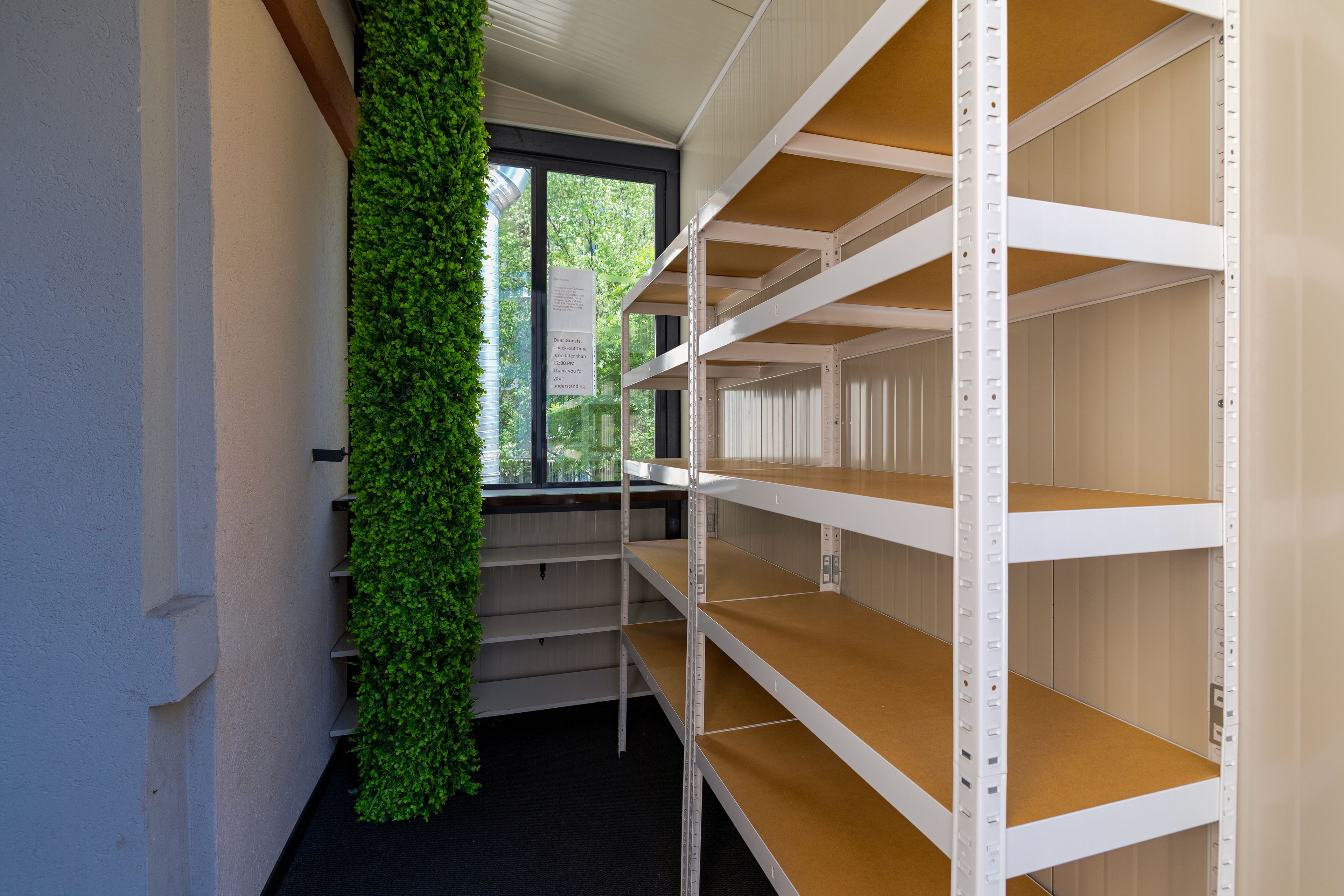 A room with white shelving units, a green vertical garden, and a window with a view of trees.
