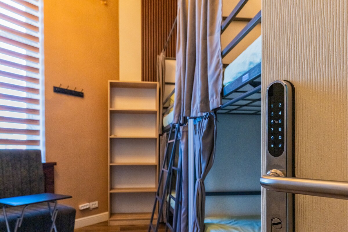A compact room with bunk beds, a foldable chair, a small table, and a wall-mounted shelf.