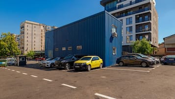 Ein Parkplatz mit mehreren Autos, einem blauen Gebäude und Wohnhäusern im Hintergrund.