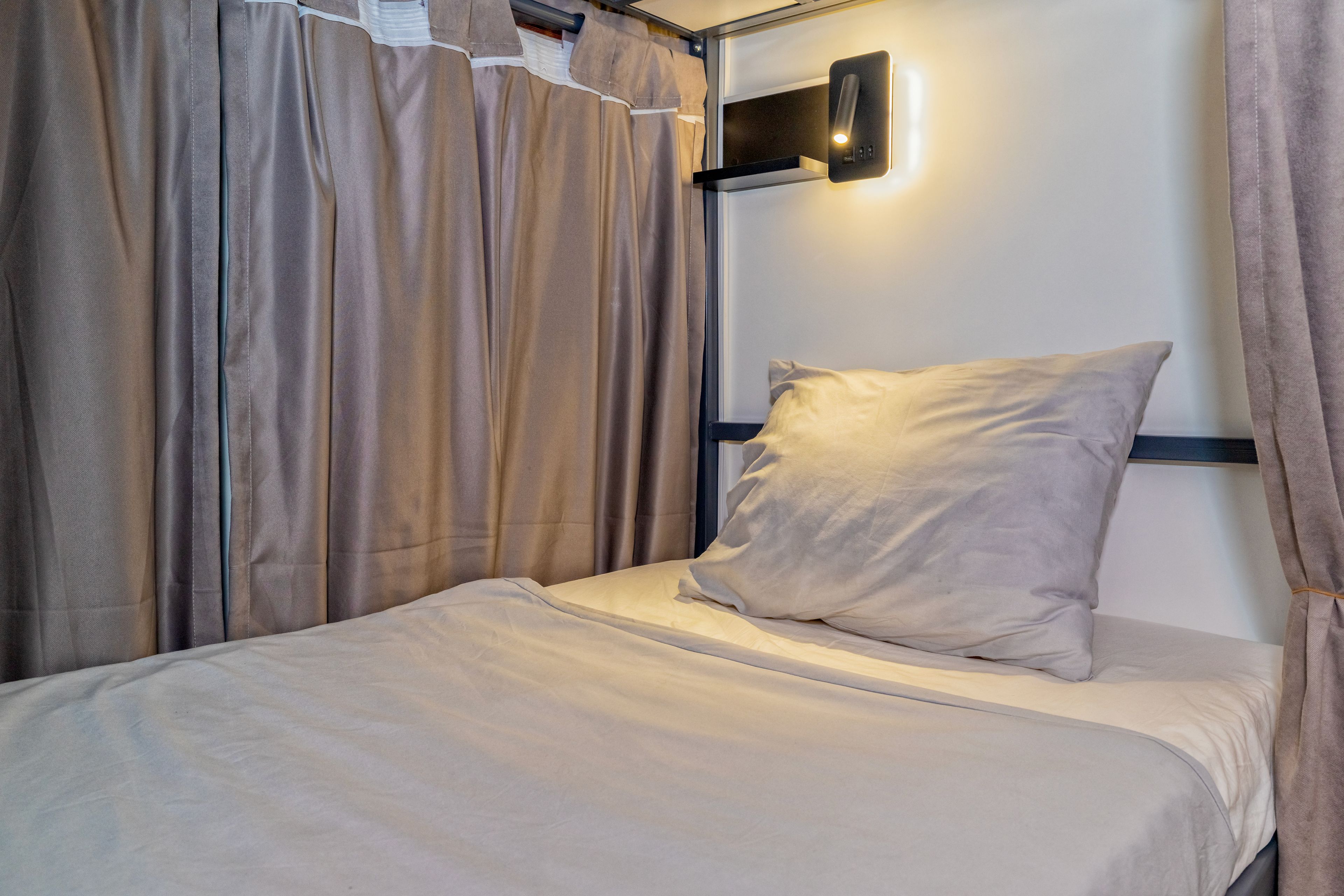 Un lit simple avec un oreiller et une tête de lit, adossé à un mur sur lequel est fixée une applique.