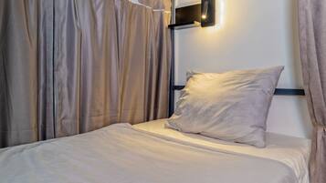 Un lit simple avec un oreiller et une tête de lit, adossé à un mur sur lequel est fixée une applique.