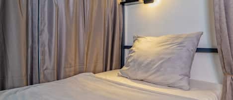 A single bed with a pillow and a headboard against a wall with a light fixture.