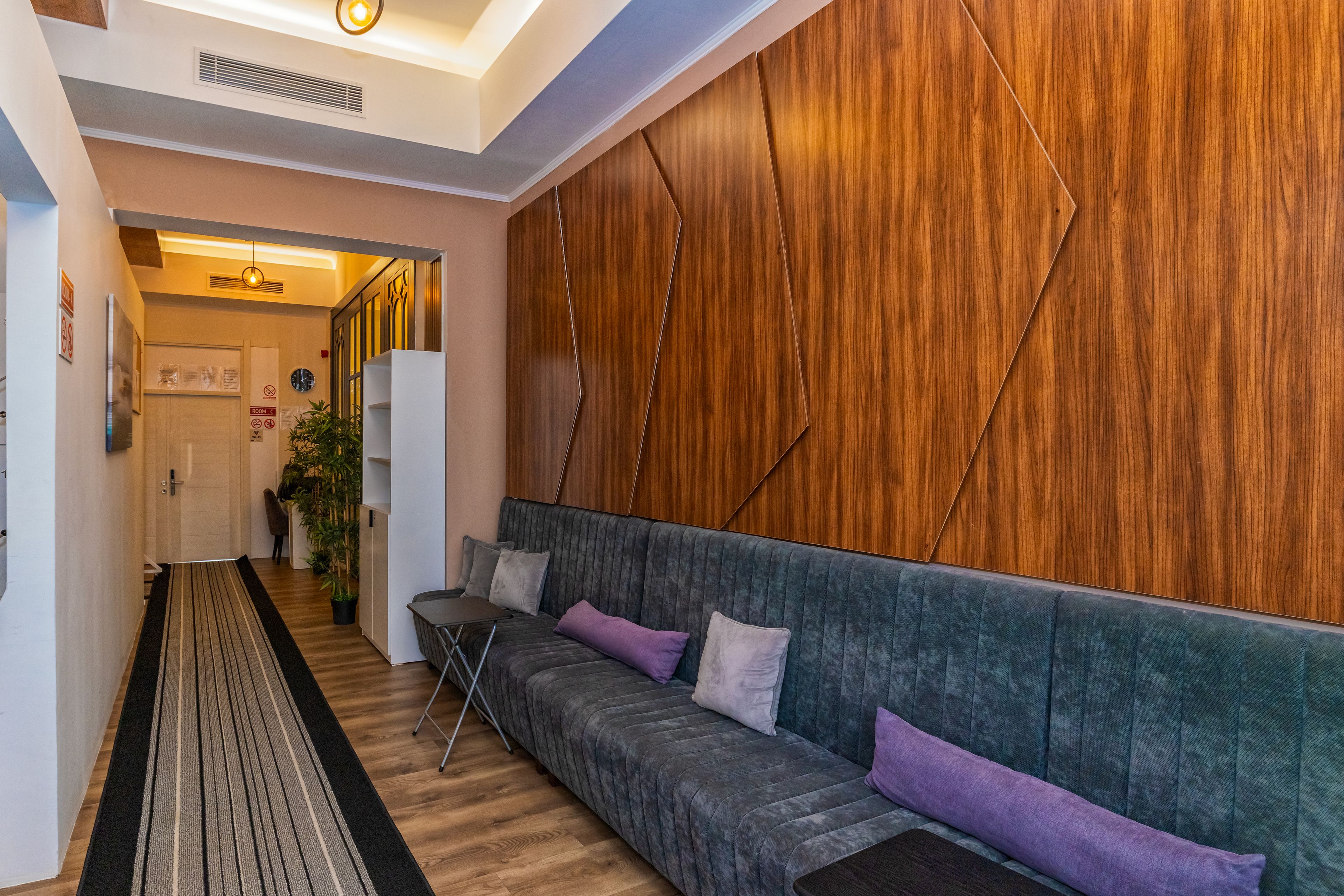 Un interior moderno con una pared de acento de madera, un sofá tapizado gris con cojines, piso de madera y un pasillo que conduce a otra habitación.