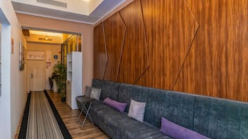 Ein modernes Interieur mit einer Wand in Holzoptik, einem grauen Polsofa mit Kissen und Holzboden. Ein Flur führt zu einem weiteren Raum.
