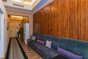 A modern interior with a wooden accent wall, a grey upholstered sofa with cushions, a wooden floor, and a hallway leading to another room. - TURQUOISE HOSTEL (Bucharest)