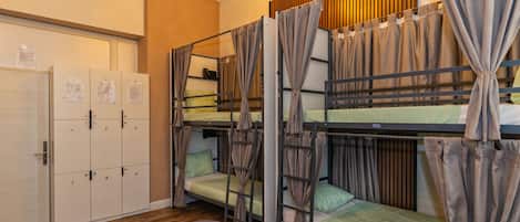 A dormitory room with bunk beds, a desk, a chair, a wardrobe, and a ceiling light fixture.