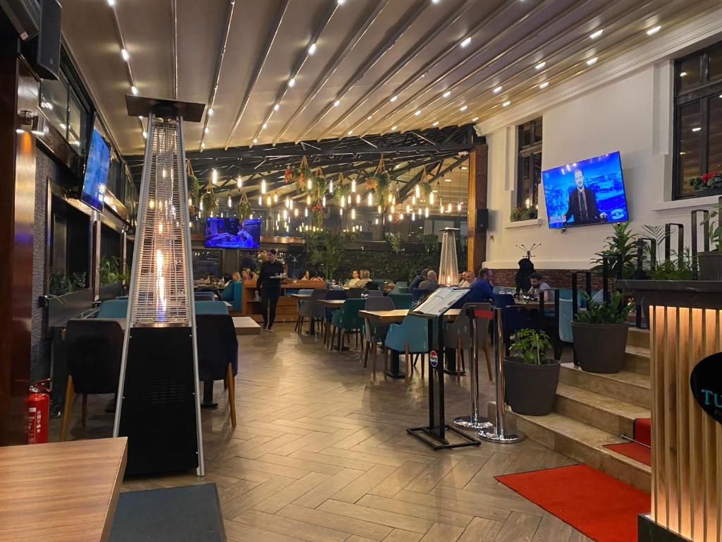 An indoor dining area with a modern design, featuring a central light fixture, multiple tables, and chairs.