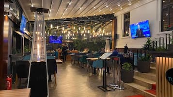Een modern ingerichte eetruimte met een centrale lamp, meerdere tafels en stoelen.