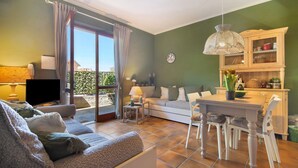 Ein Wohnzimmer mit einer Couch, einem Esstisch mit Stühlen, einem Fernseher und einer Vitrine mit Dekoration.