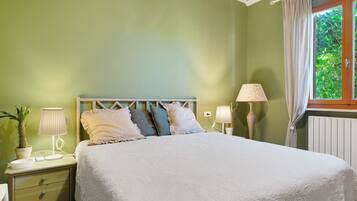 Une chambre à coucher avec un lit, deux tables de chevet, une fenêtre avec des rideaux et une plante en pot.
