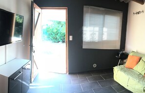 A room with a TV, a sofa, a window with blinds, and a door leading outside.