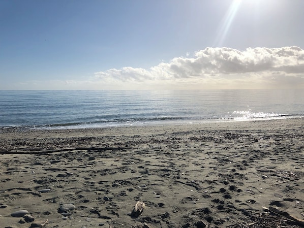 Une plage avec un ciel dégagé, une mer calme et quelques rochers éparpillés.