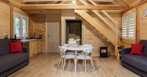 Acogedor interior de cabaña con una mesa de comedor, dos sofás, una zona de cocina y una escalera.
