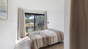 A bedroom with a bed, a large window, and a view of greenery outside. - Villa con piscina, aire acondicionado y vistas al mar (Pineda Pals)