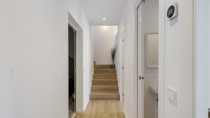 A hallway with wooden flooring, white walls, a staircase, and a door with a light switch. - Villa con piscina, aire acondicionado y vistas al mar (Pineda Pals)