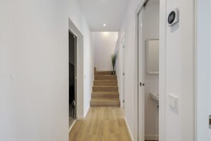A hallway with wooden flooring, white walls, a staircase, and a door with a light switch.