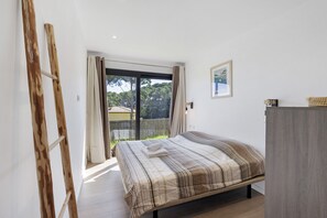 A bedroom with a bed, a wooden ladder, a window with curtains, a framed picture, and a grey wardrobe.