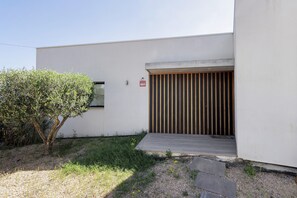 A modern building with a white exterior, a wooden door, and a small garden area with a tree and gravel path.