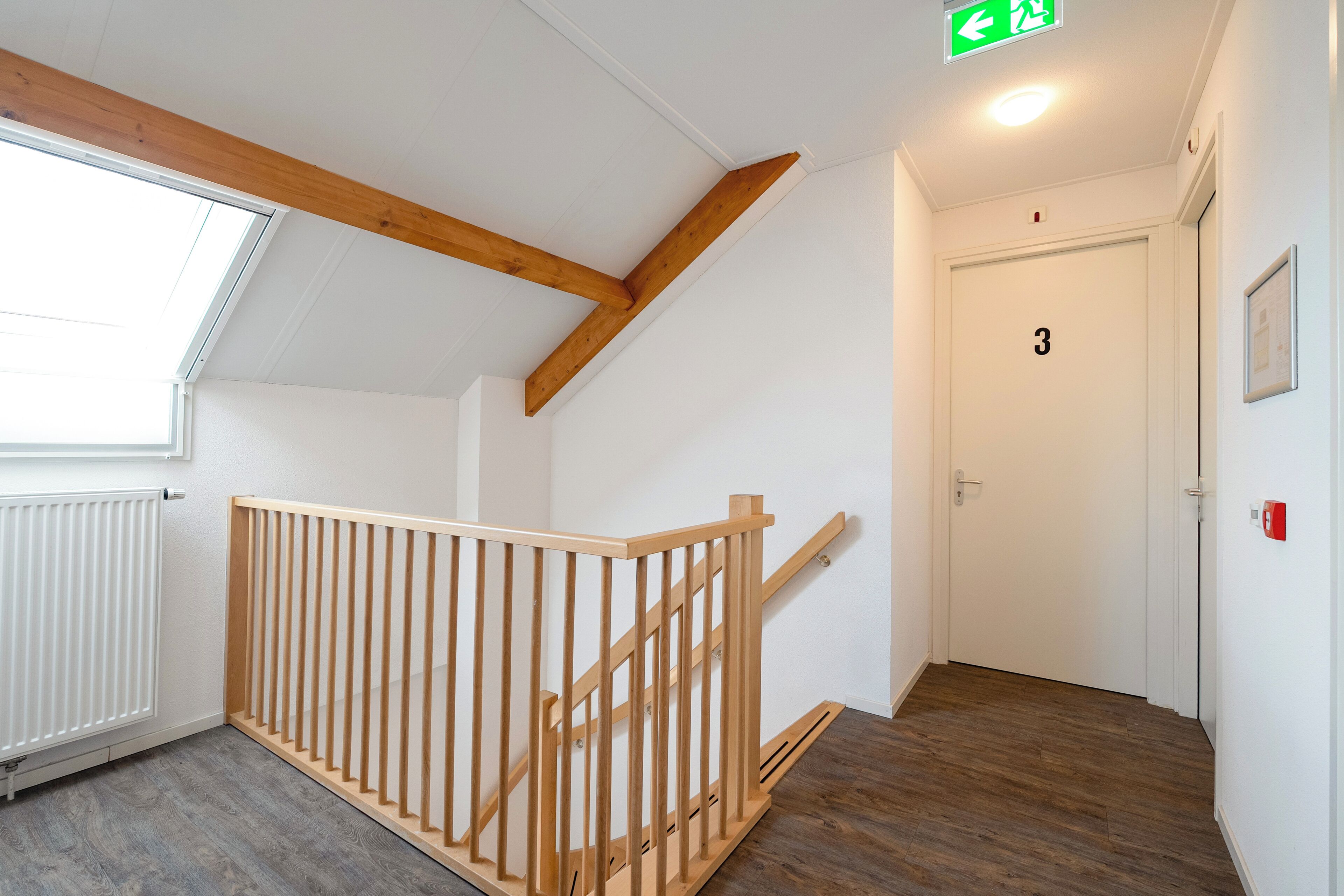 A staircase with wooden railings, a white door with the number 3, and a window with a white radiator.