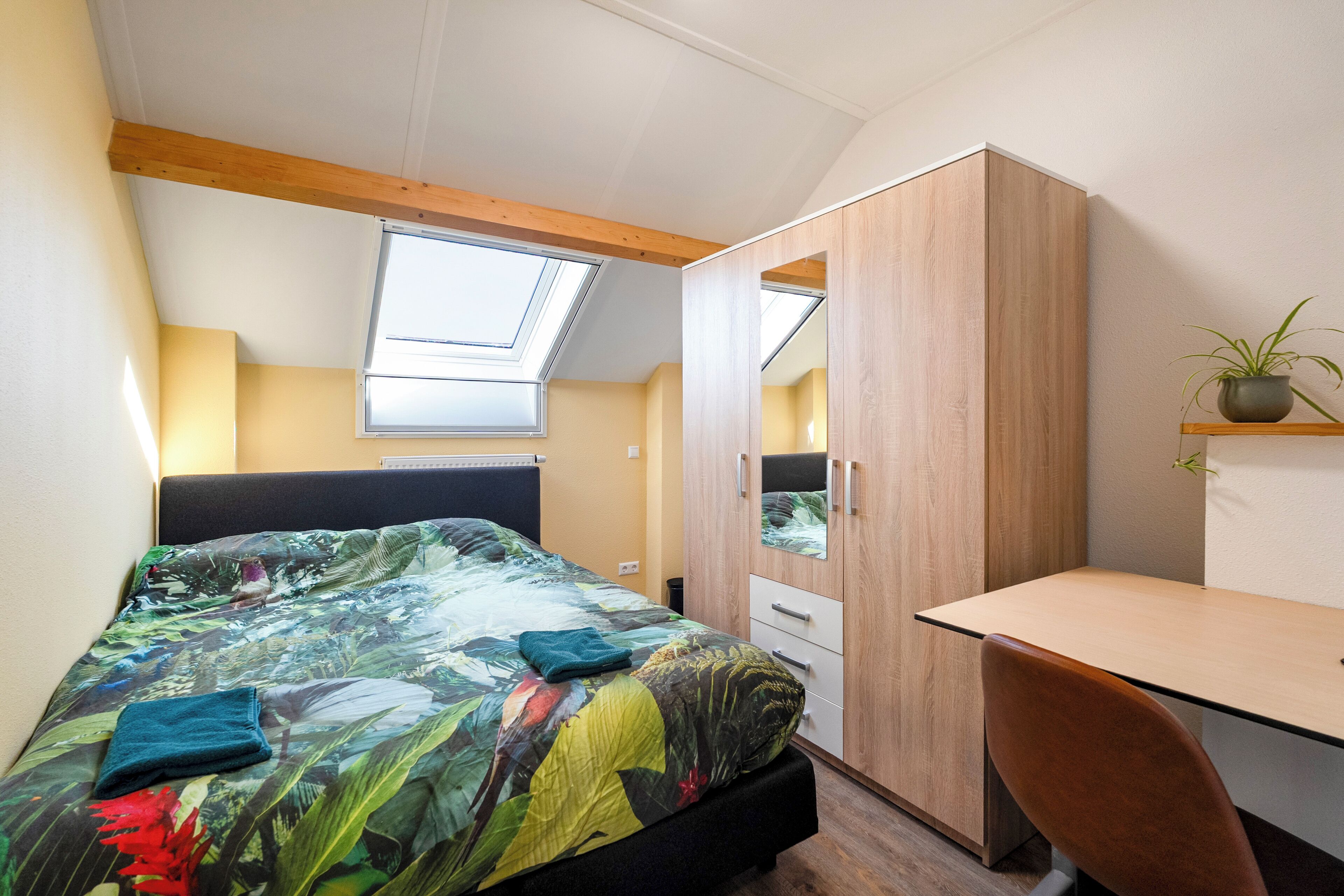 Een slaapkamer met een bed, een bureau, een kledingkast en een dakvenster.