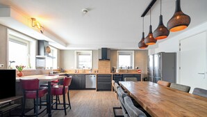 Cozinha moderna com mesa de jantar de madeira, banquetas e iluminação pendente.