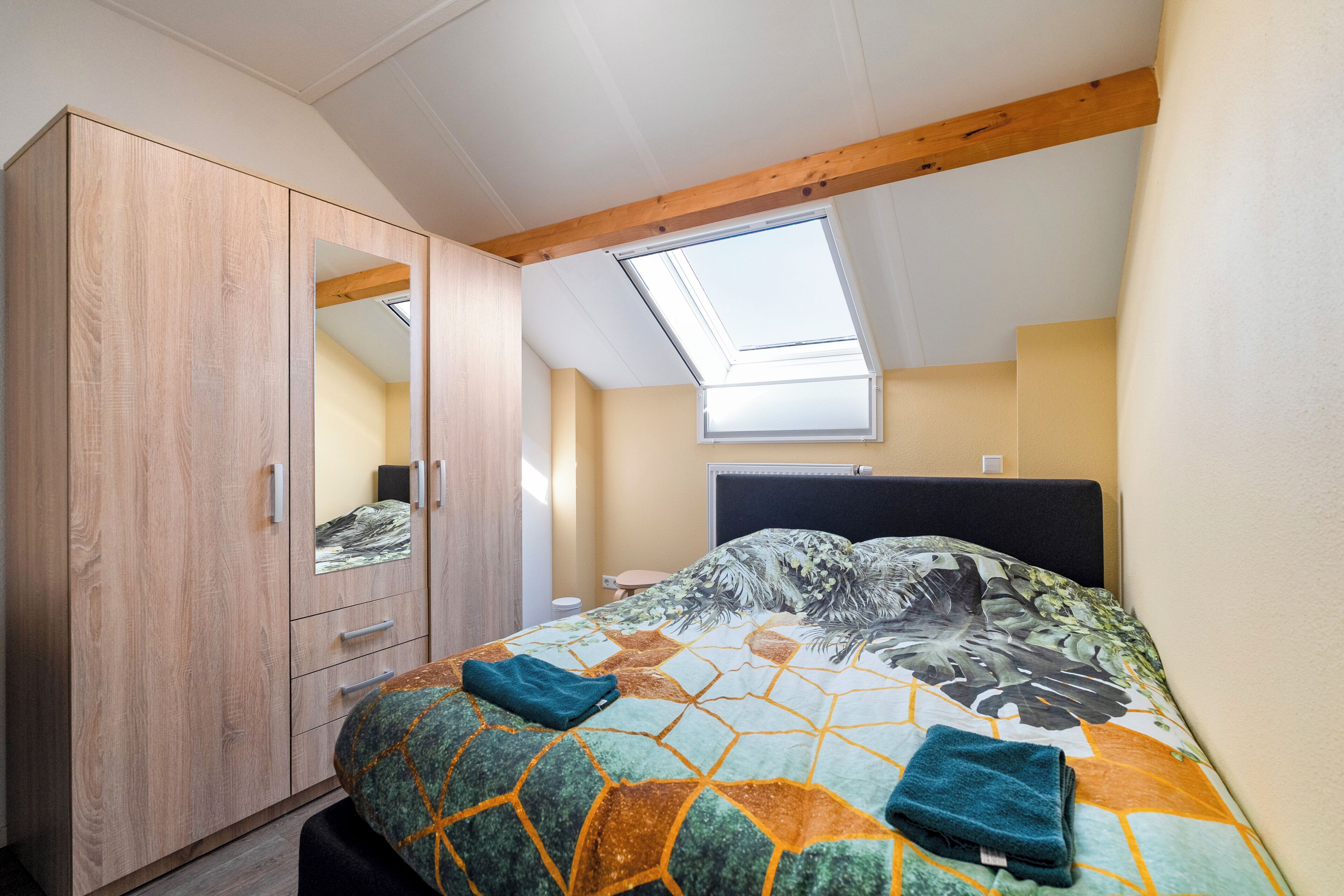 A bedroom with a bed, a wardrobe, a skylight, and a window.