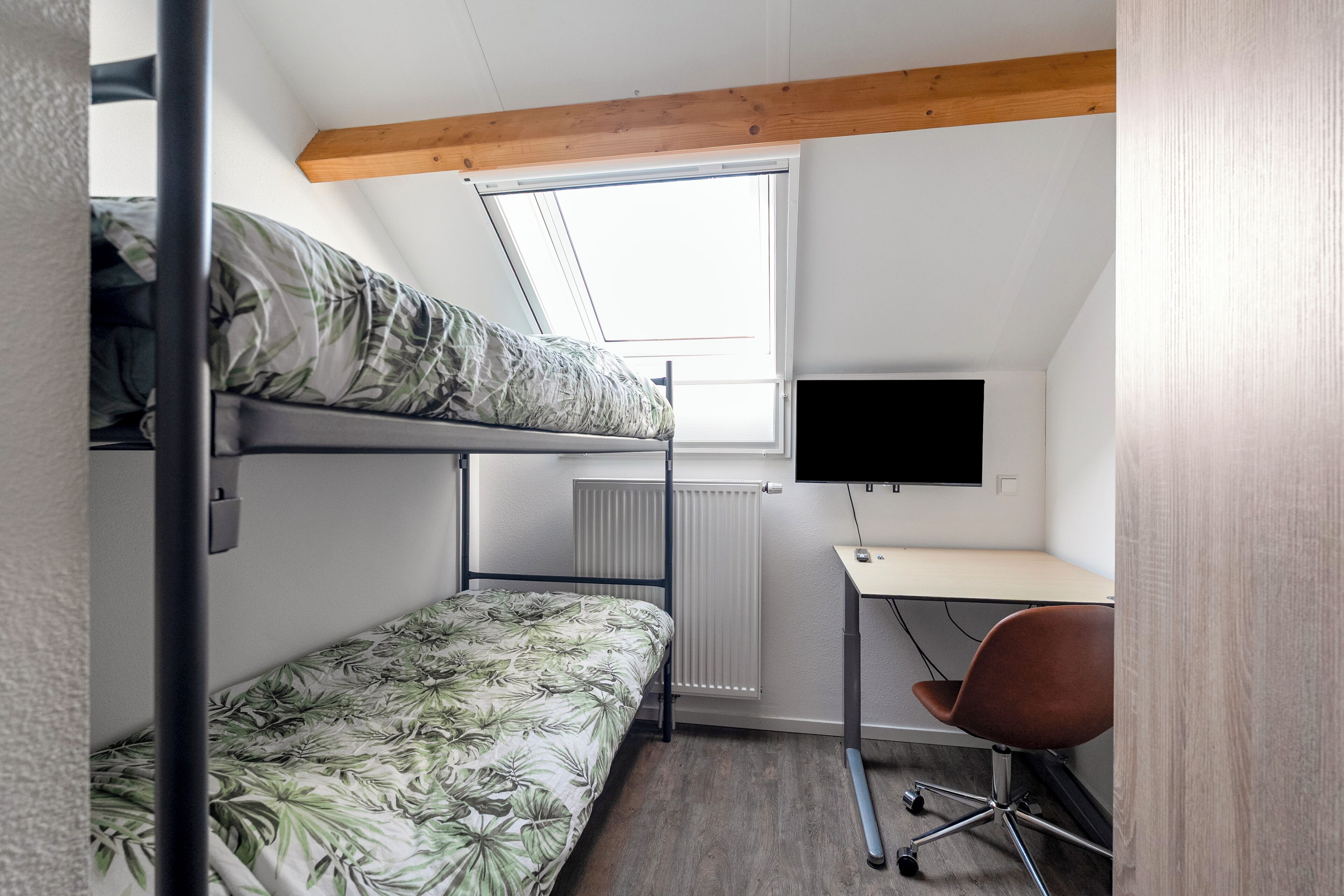 Een studentenkamer met stapelbedden, een bureau met een computer en een raam.