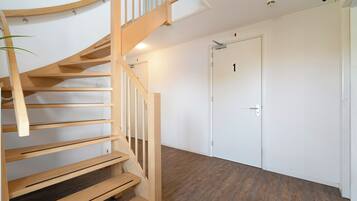 Un escalier en colimaçon en bois menant à un palier, une porte blanche avec un numéro, et un plancher en bois.