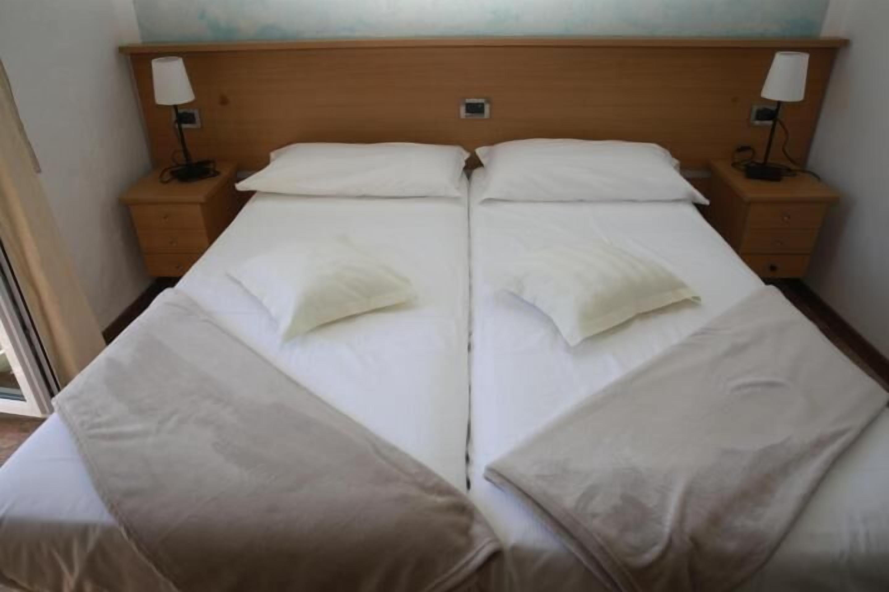 Un lit double avec deux tables de chevet, chacune équipée d’une lampe, dans une chambre dont la tête de lit est en bois.