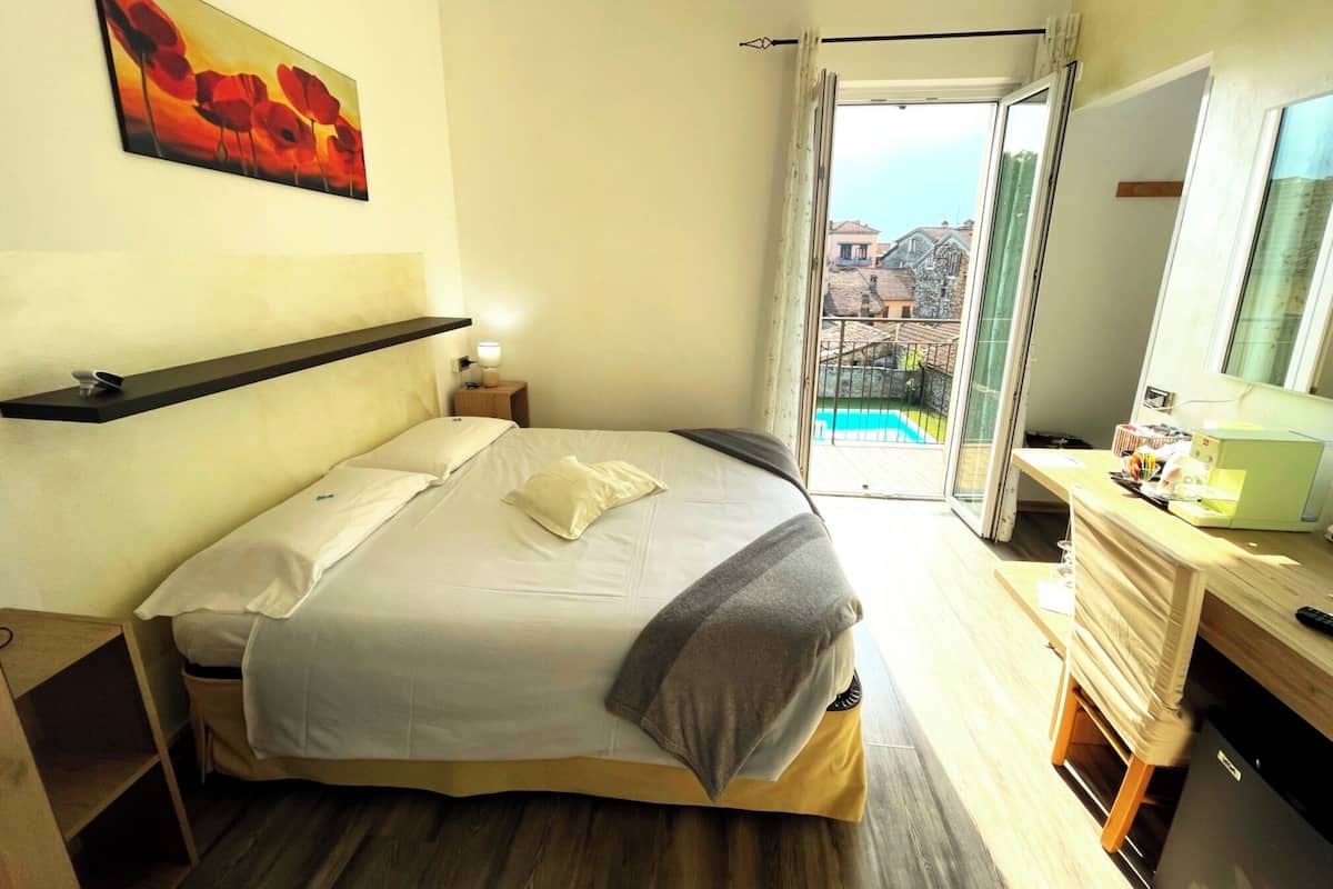 Un dormitorio con cama, mesita de noche, lámpara y un cuadro en la pared.