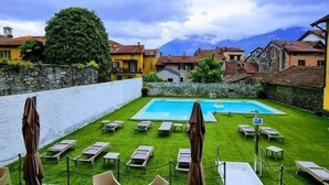 Un espace piscine doté de chaises longues et de parasols, entouré de bâtiments et avec une montagne en toile de fond.