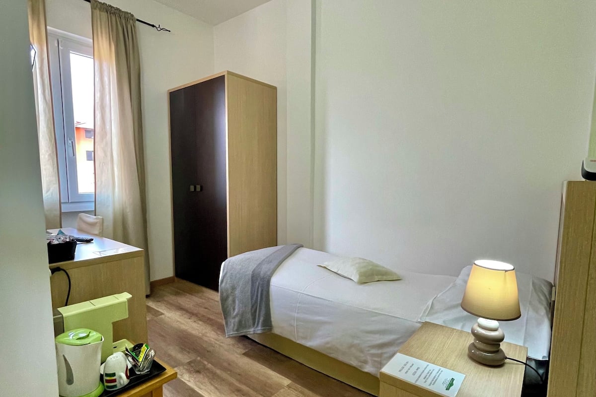 Una habitación de hotel con cama, escritorio, armario y una pequeña mesa con lámpara.