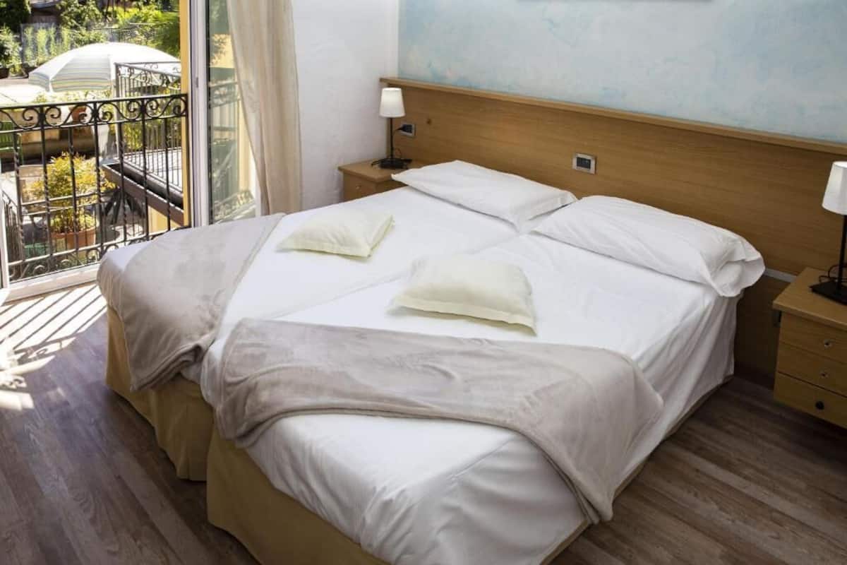 Una habitación de hotel con una cama grande, cabecera de madera, mesitas de noche y un balcón con vistas.