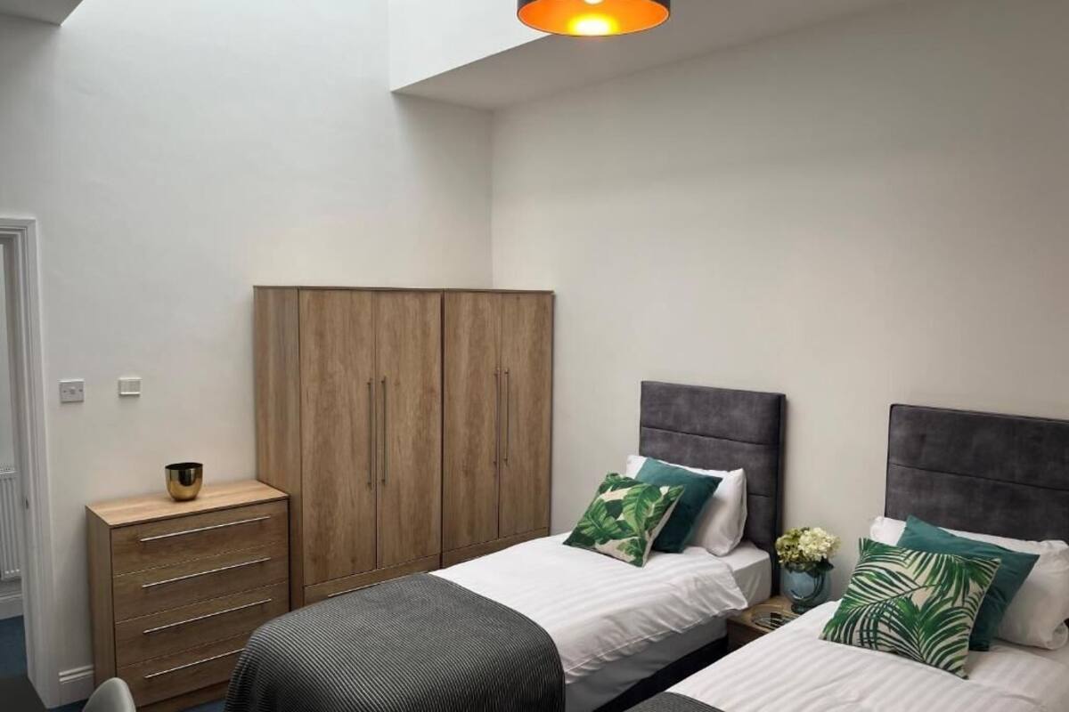 Un dormitorio con dos camas, un armario, una mesita de noche con lámpara y vistas al cielo.