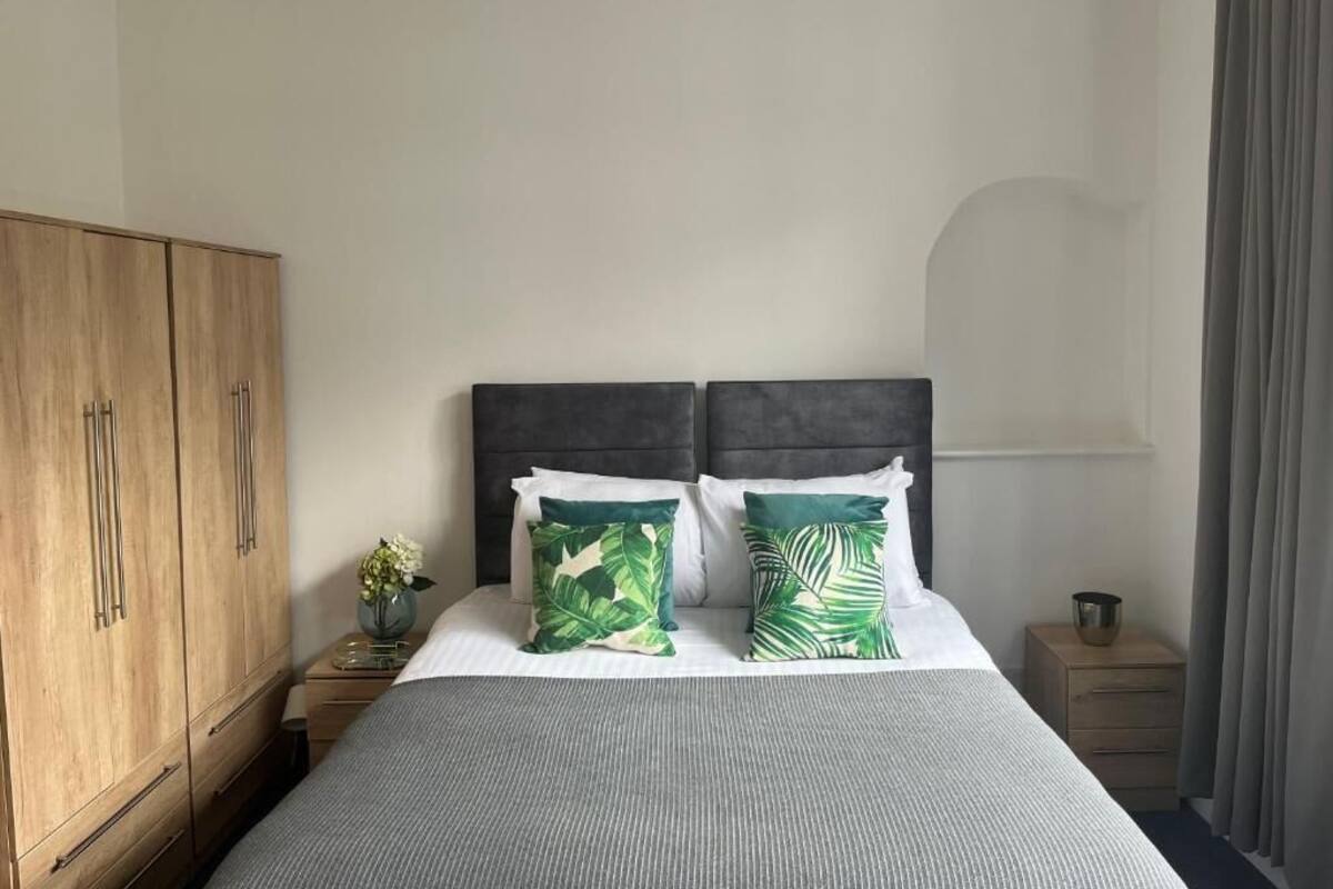 Un dormitorio con una cama, dos almohadas, una mesita de noche, un armario de madera y una ventana con cortinas.