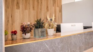 A reception desk with a wooden backdrop, various potted plants, and a white reception counter. - HOTEL GOLDEN (San Sebastián de los Reyes)