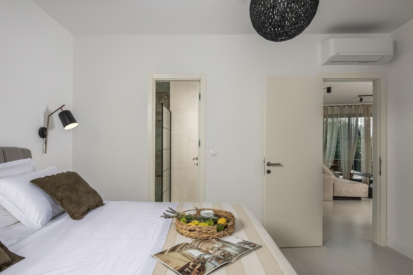 A bedroom with a bed, bedside lamp, open door to a balcony, and a basket of fruits on the nightstand.