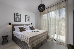 A modern bedroom with a bed, a bedside table, a hanging light fixture, and a large window with sheer curtains. - Villa Medellin ZadarVillas (Pridraga)