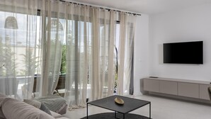 Ein modernes Wohnzimmer mit einer Couch, einem Couchtisch, einem Fernseher und einem Balkon mit transparenten Vorhängen.