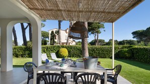An outdoor patio with a table and chairs, a hanging light fixture, and a view of a house and greenery. - House Next to Golf Course, 800 m from Platja de Pals (Pals)