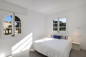 A bedroom with a bed, two windows, a nightstand, and a view of palm trees. - House Next to Golf Course, 800 m from Platja de Pals (Pals)