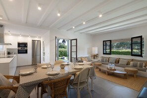 A modern kitchen with built-in appliances, a dining area with a table set for four, and a living room with a sofa and a window. - House Next to Golf Course, 800 m from Platja de Pals (Pals)