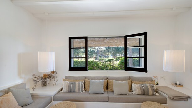 A modern living room with a sofa, two side tables, a window with open shutters, and a view of greenery. - House Next to Golf Course, 800 m from Platja de Pals (Pals)