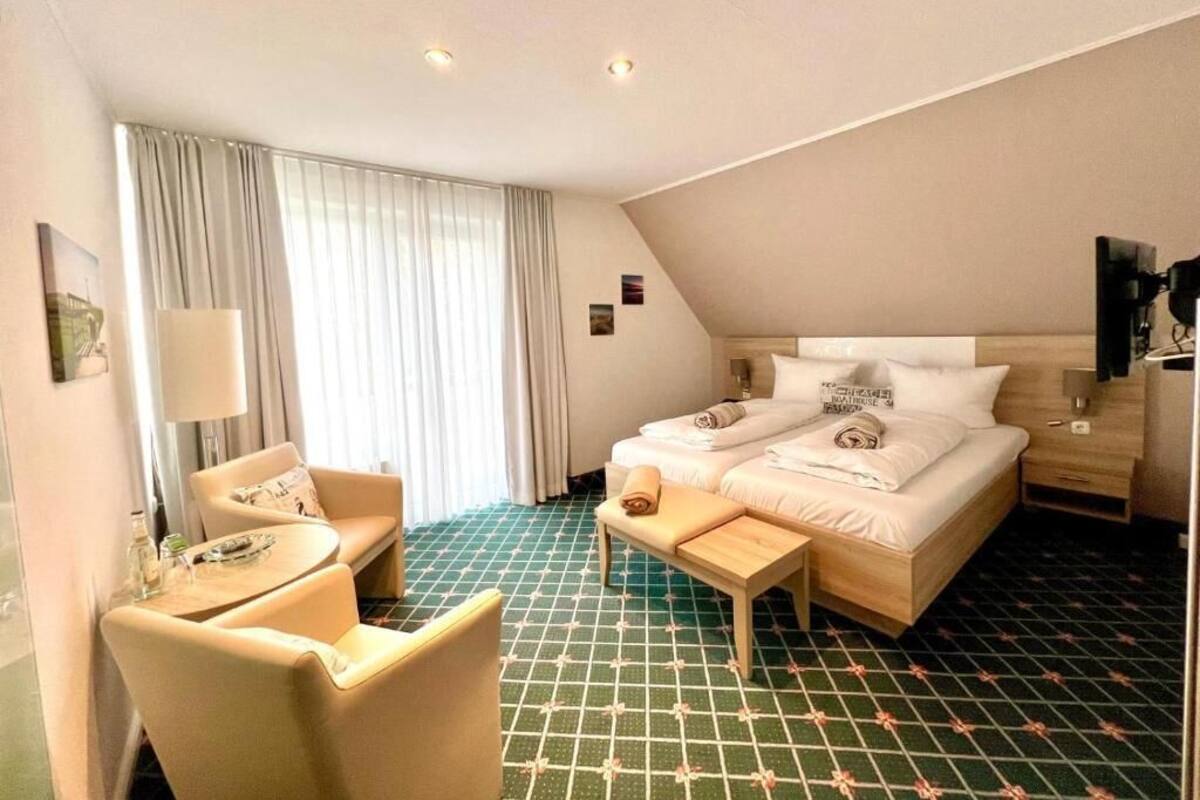 Ein Hotelzimmer mit Bett, Stuhl, kleinem Tisch, Lampe und einem Fenster mit Vorhängen.