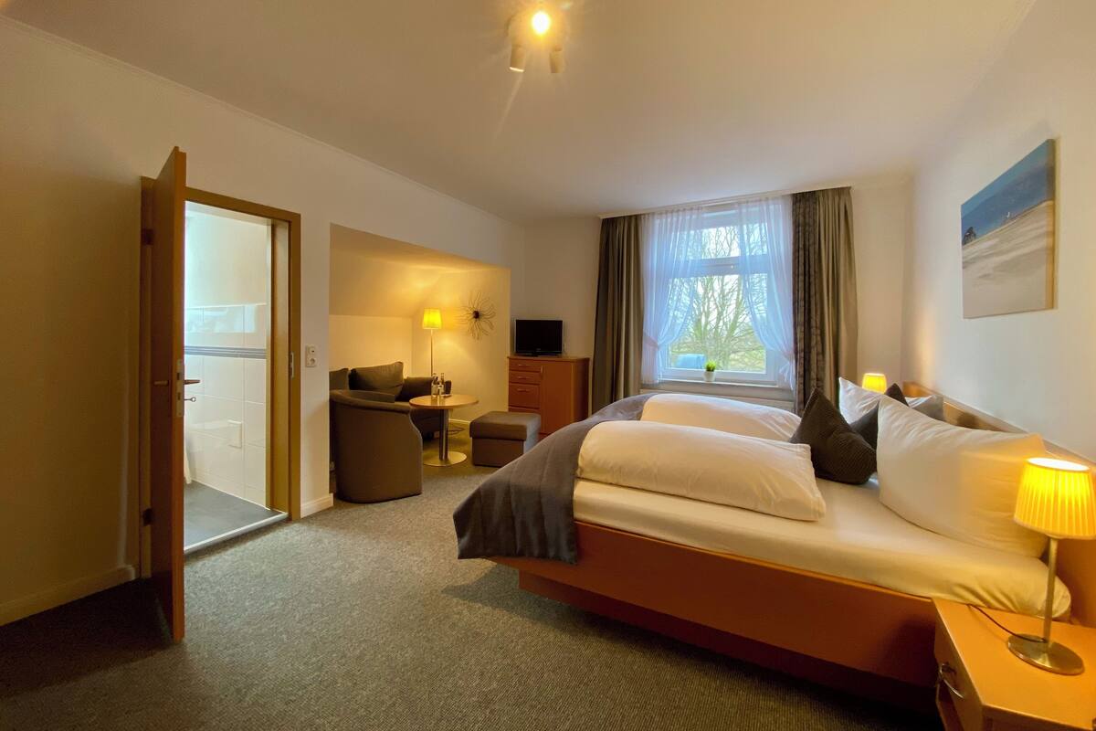 Ein Hotelzimmer mit Bett, Schreibtisch, Stuhl, Fernseher und einem Fenster mit Vorhängen.