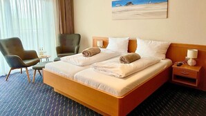 Een hotelkamer met een bed, twee stoelen, een nachtkastje, een lamp en een schilderij aan de muur.